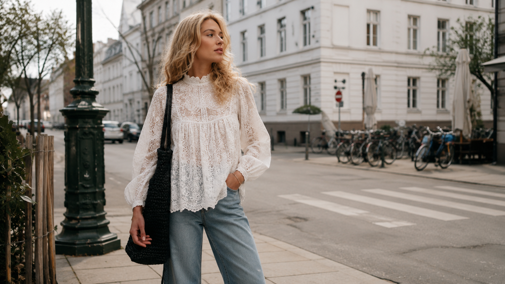 Жена с бял дантелен топ и светлосини дънки на градска улица в стил Copenhagen street style.