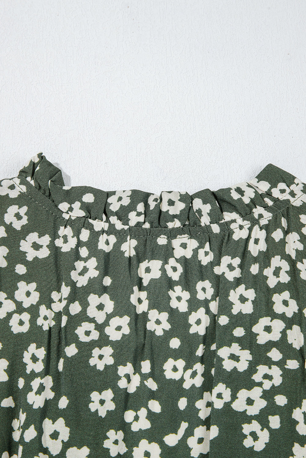 Green floral patterned fabric with small white flowers and ruffled neckline detail