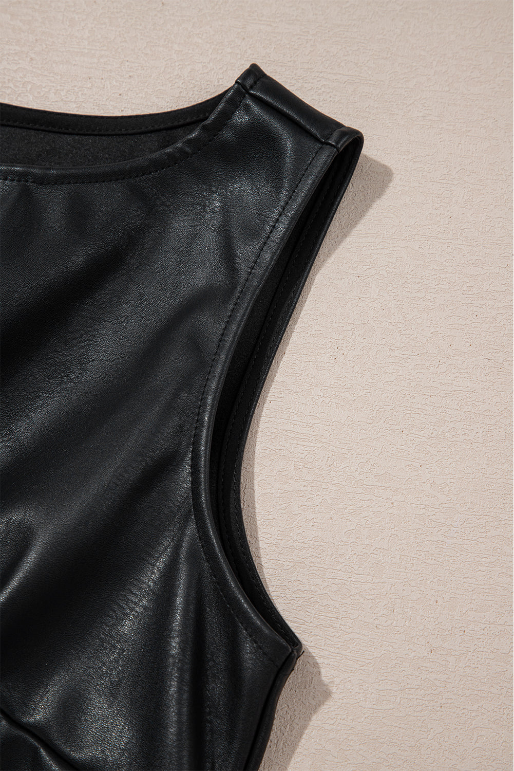 Close-up of black faux leather sleeveless top on beige textured background
