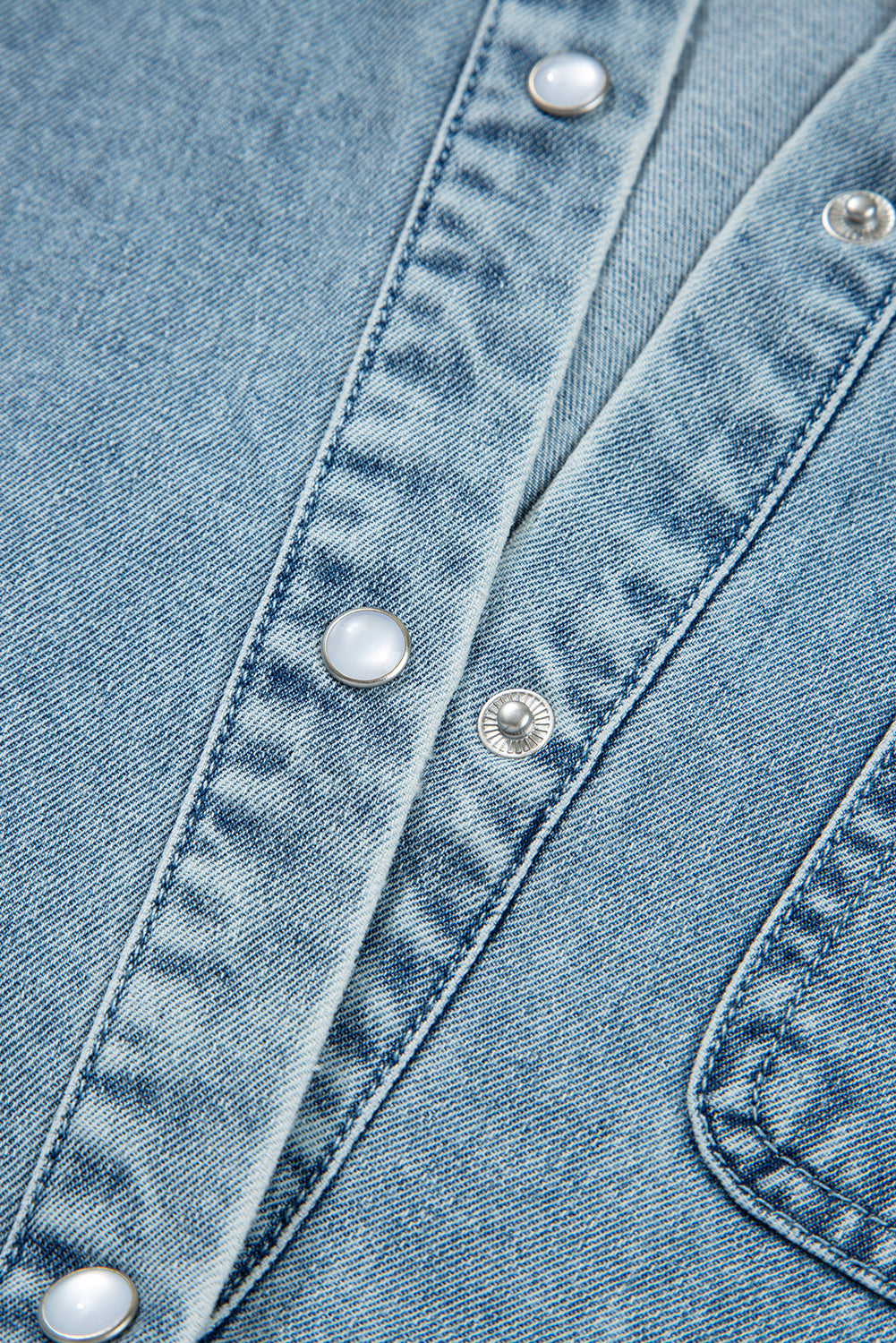 Close-up of light blue denim fabric with metal snap buttons and pocket stitching