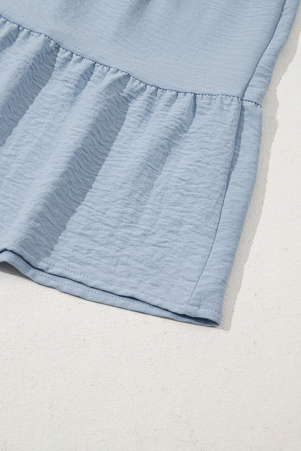 Light blue ruffled hem dress closeup with textured soft fabric on a neutral background