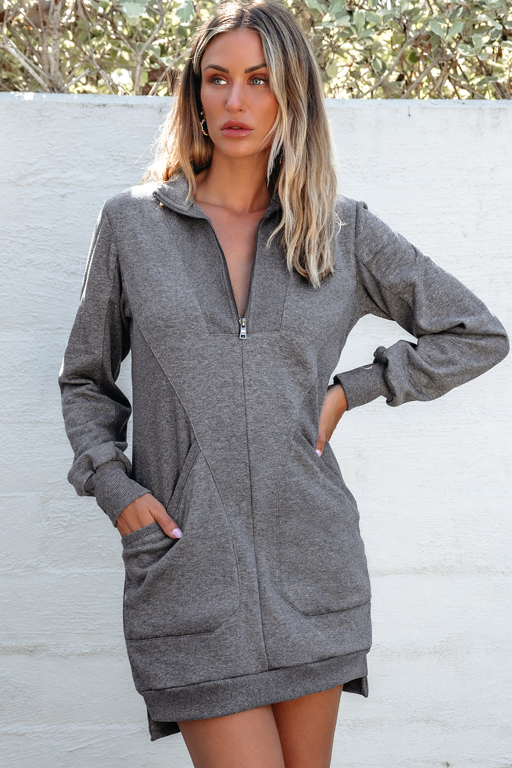 Woman wearing a grey zip-up sweatshirt dress with pockets, outdoor casual fashion
