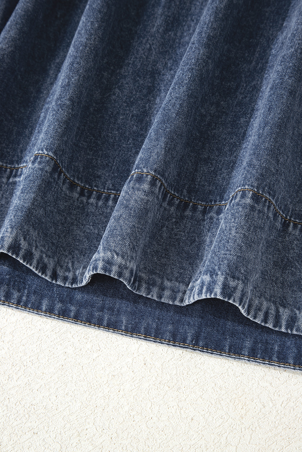 Close-up of blue denim skirt hem with visible stitching and textured fabric