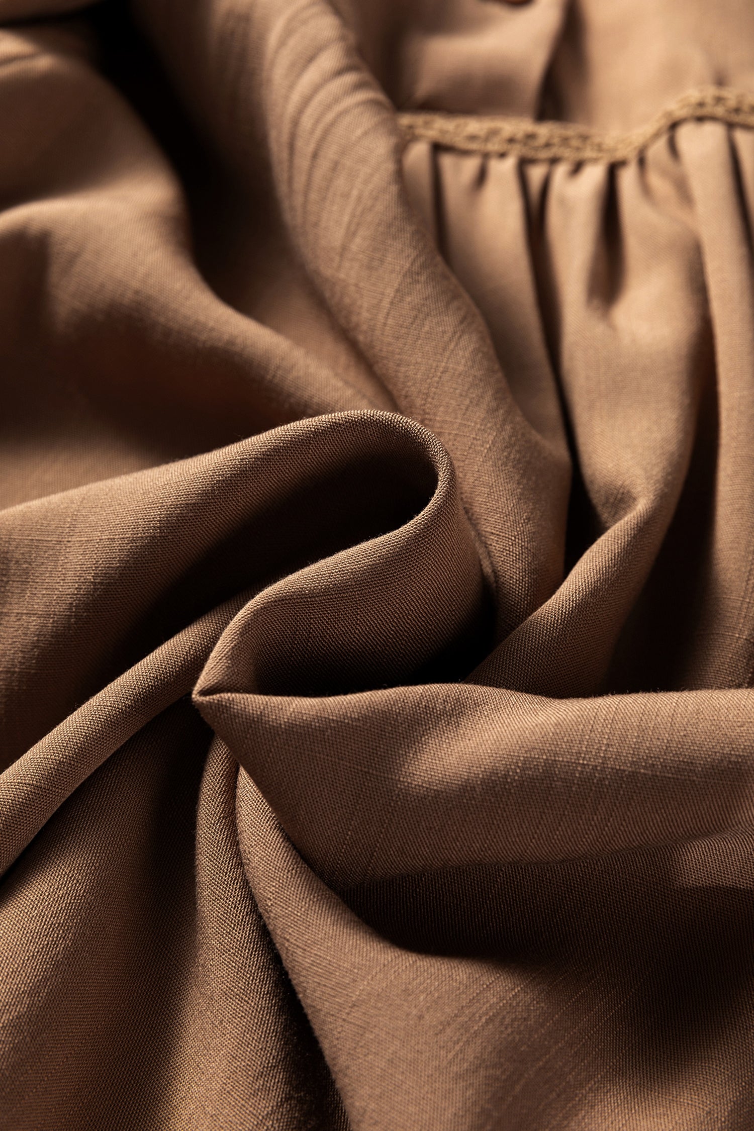 Close-up of brown soft fabric with gentle pleats and stitched detail