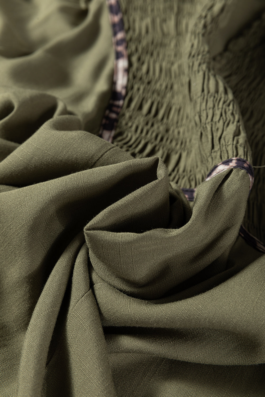 Close-up of olive green ruched fabric with soft texture and patterned trim detail