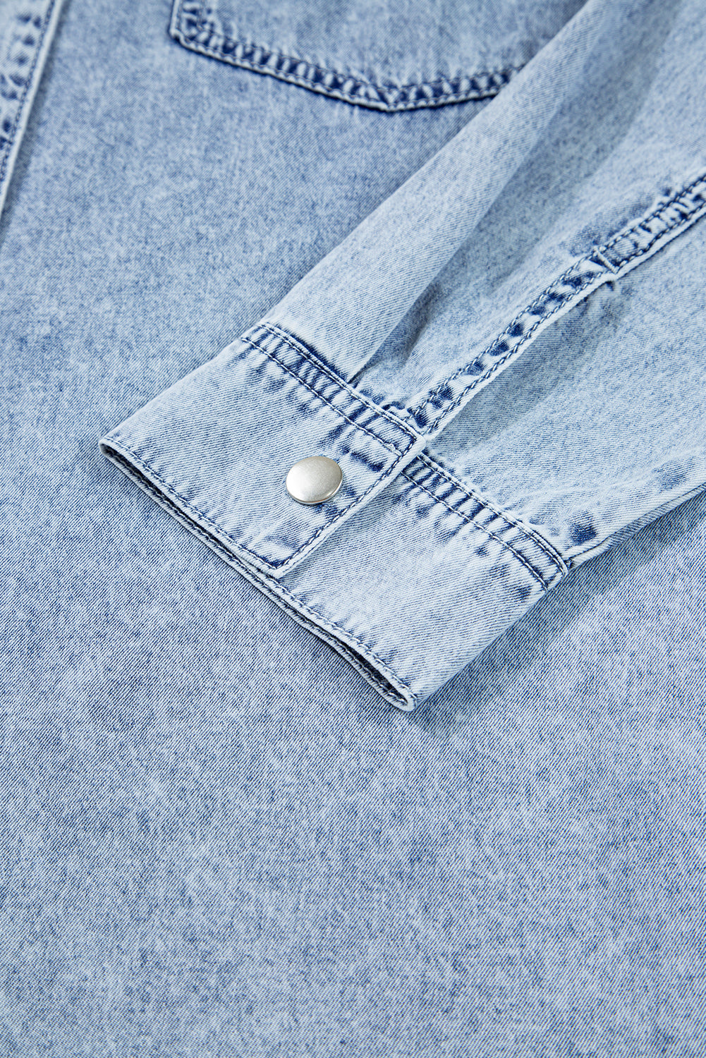 Light blue denim shirt sleeve with metal snap button and visible stitching detail