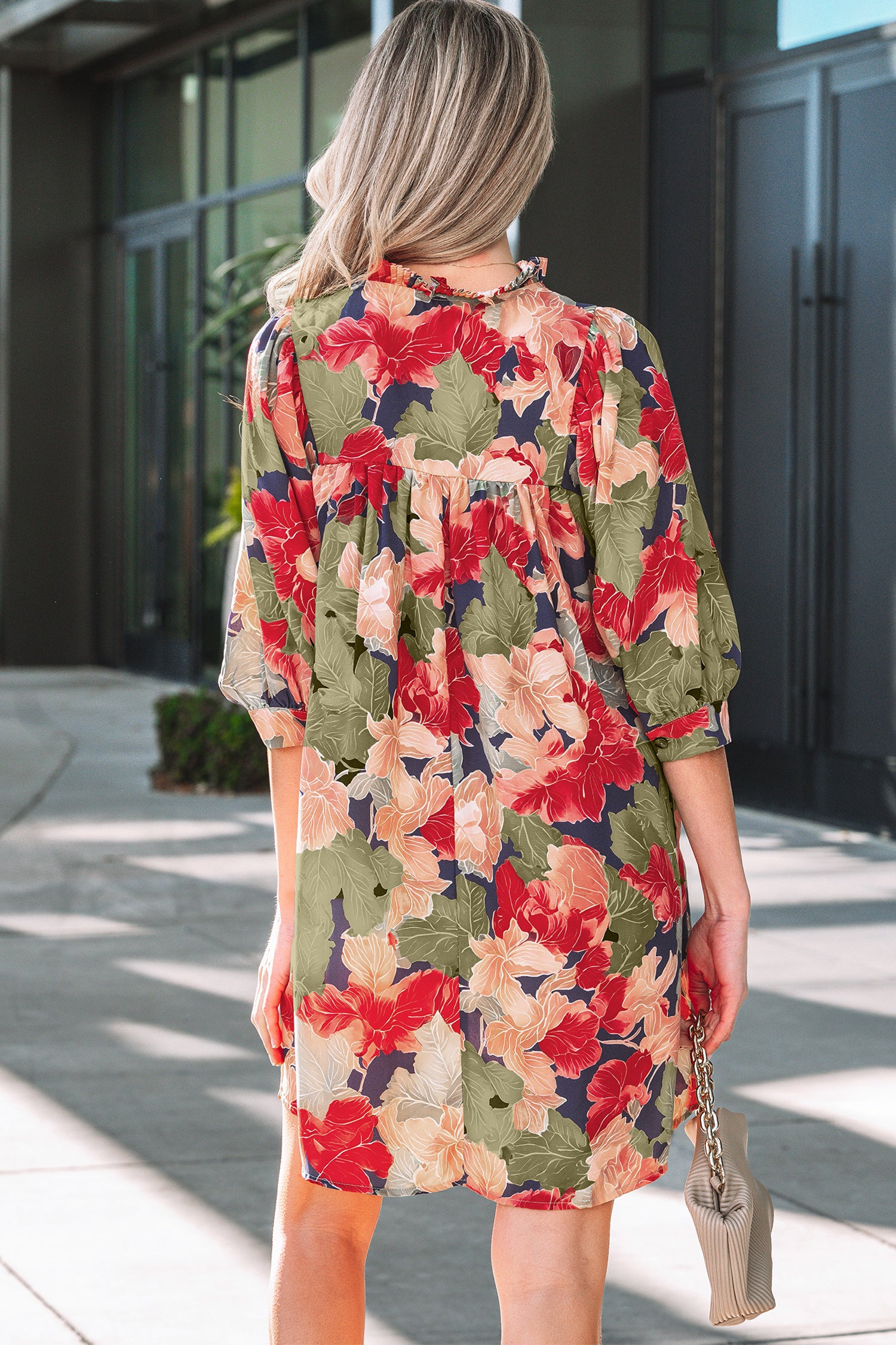 Woman in a loose floral dress with red, green, and beige patterns, holding a beige purse