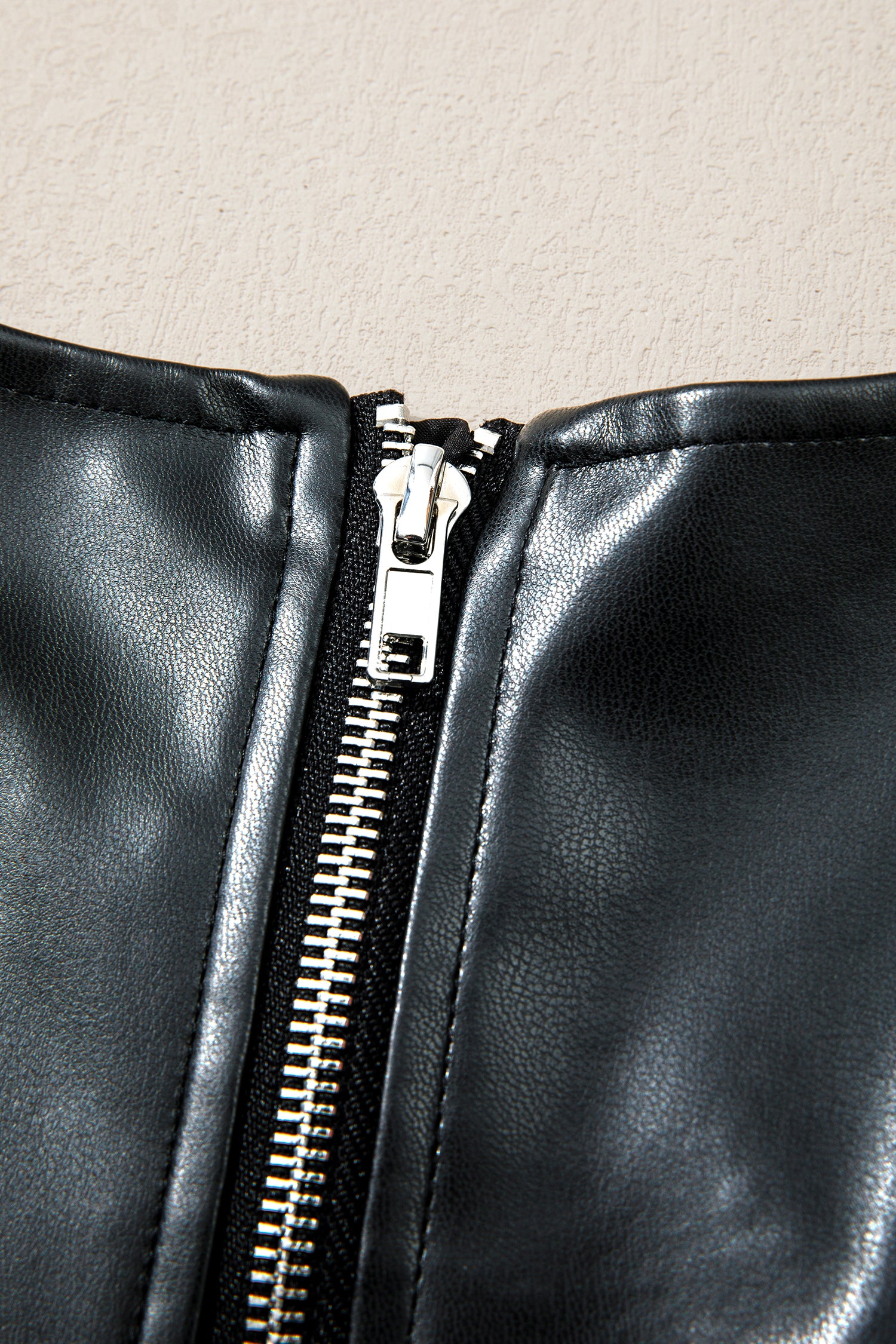 Close-up of black faux leather garment with silver zipper detail
