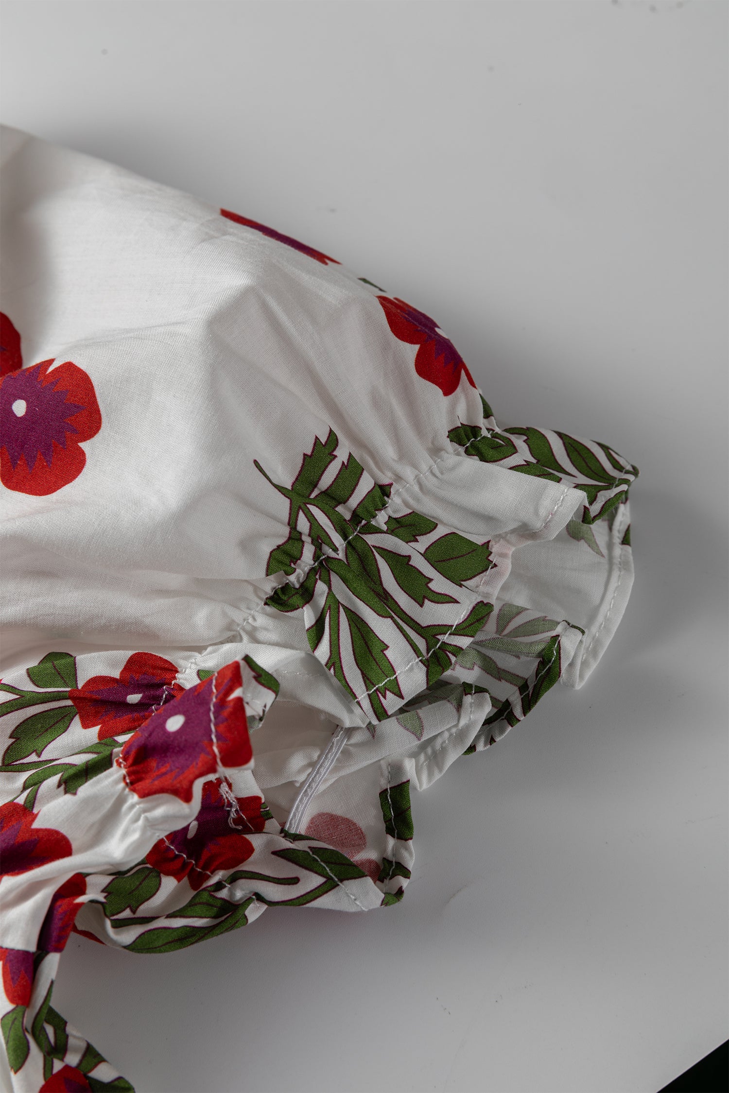 White fabric with red floral print and green leaves, gathered sleeve detail