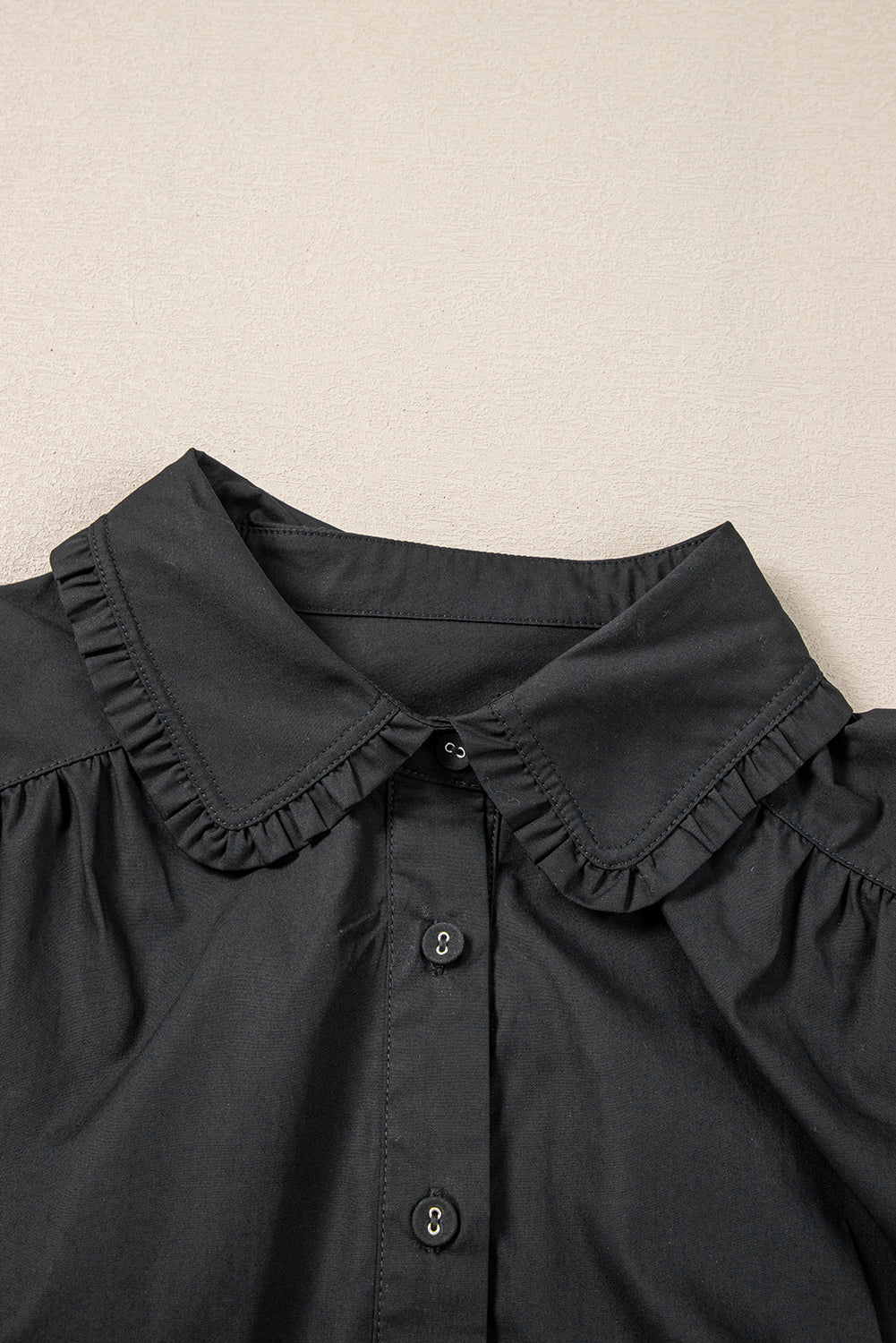 Black blouse with ruffled collar and front buttons on neutral background