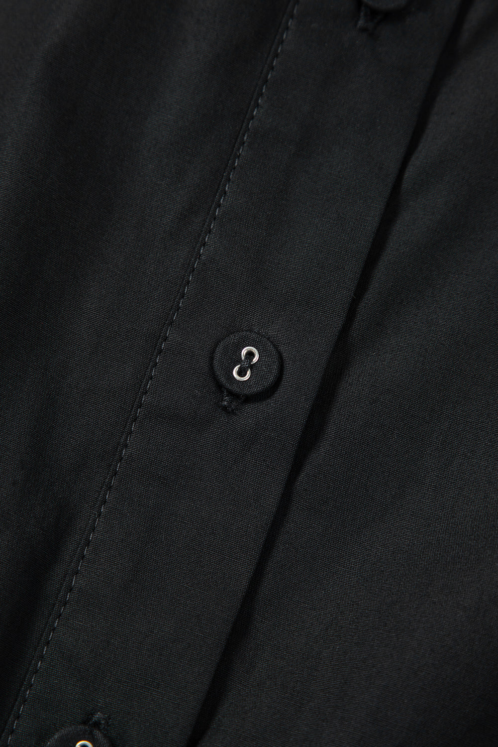 Close-up of black shirt fabric with button and detailed stitching