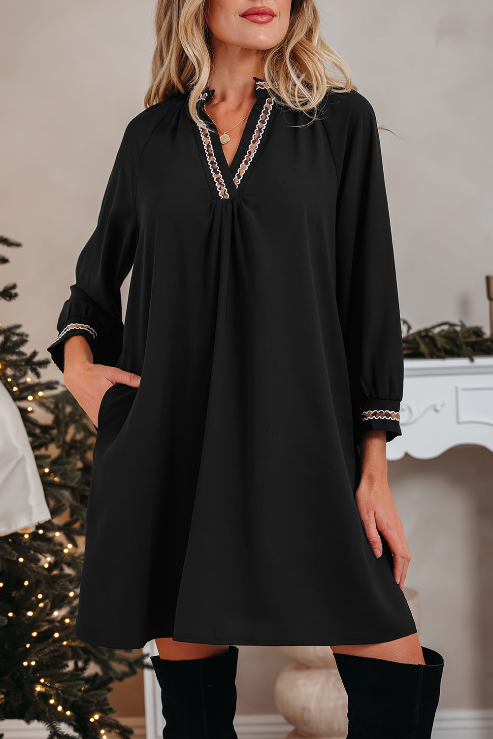 Woman wearing black long sleeve mini dress with embroidered trim and pockets, holiday decor