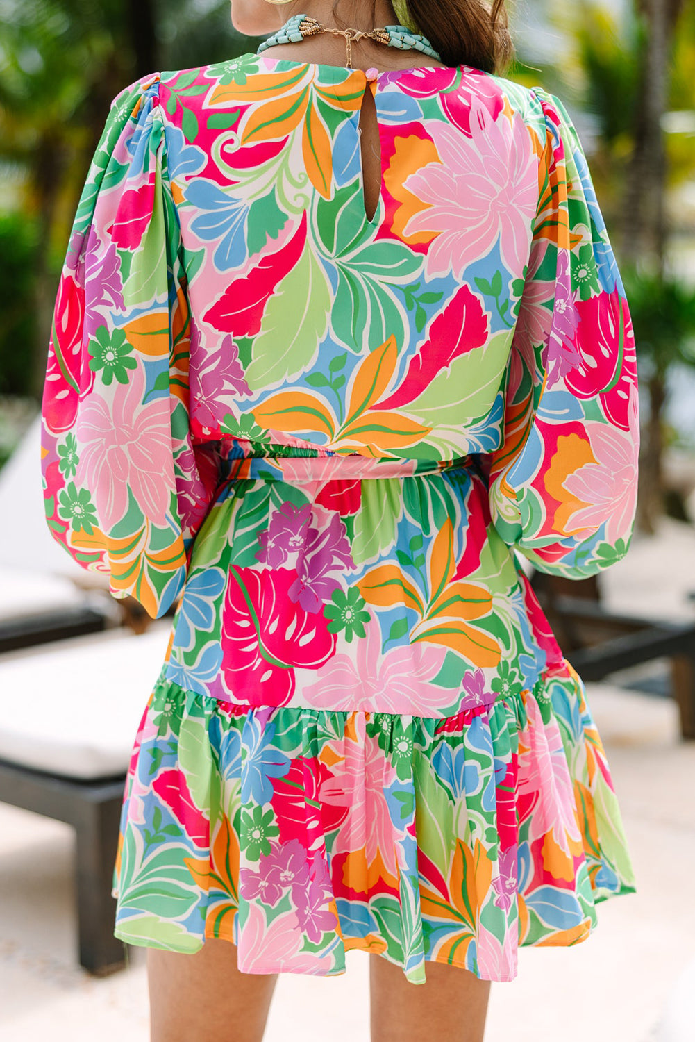 Woman wearing a bright floral mini dress with puff sleeves, tropical outdoor setting