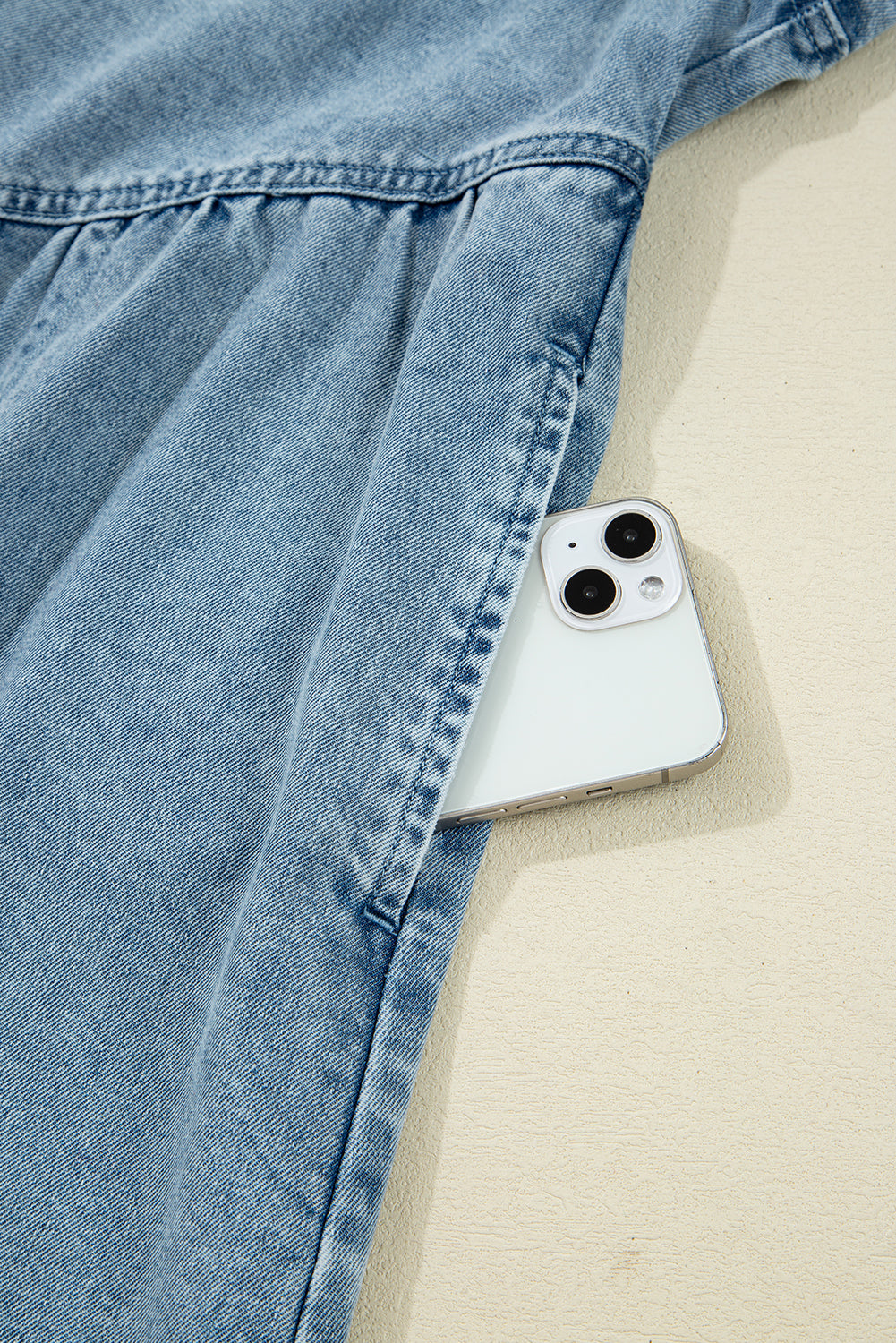 Light blue denim dress with a smartphone in the side pocket on a beige surface