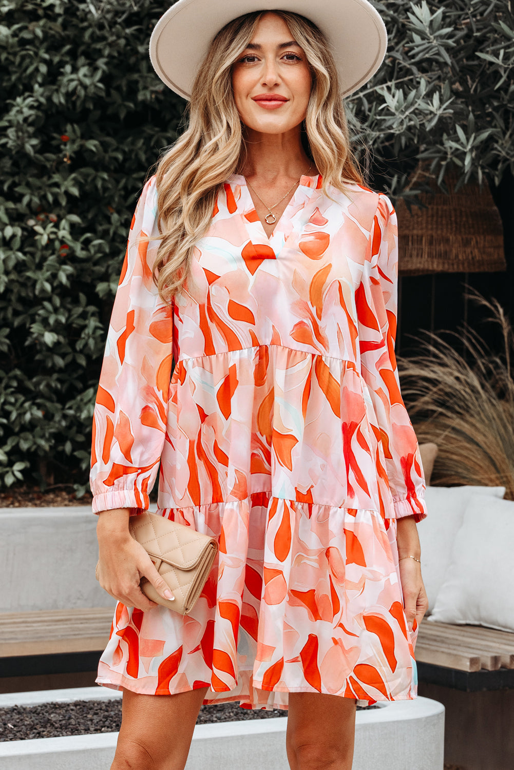 Woman in a colorful floral print long sleeve dress with hat and beige clutch outdoors