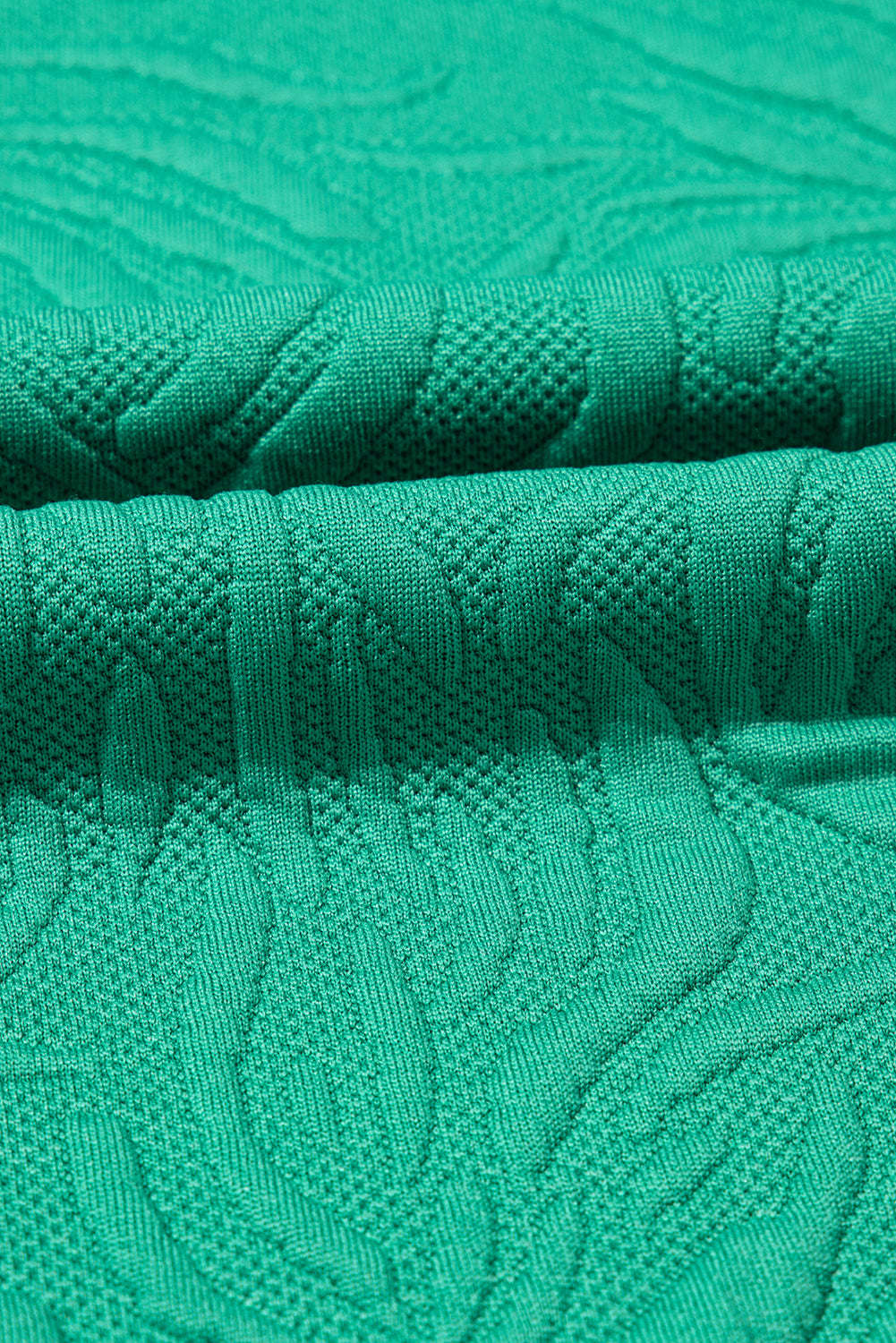 Close-up of textured green knit fabric with raised pattern, soft and detailed textile