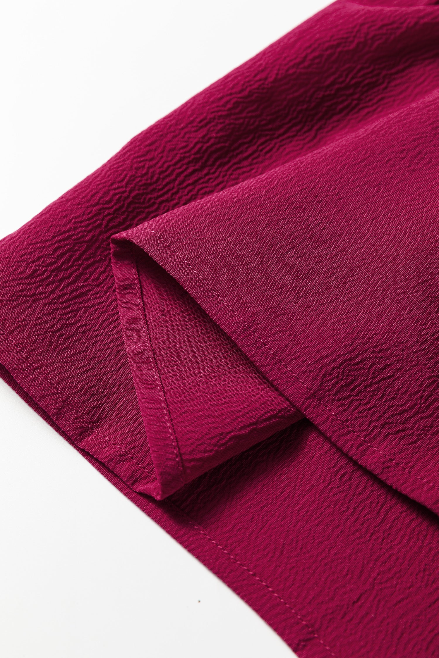 Close-up of textured magenta fabric with visible stitching and folded edge
