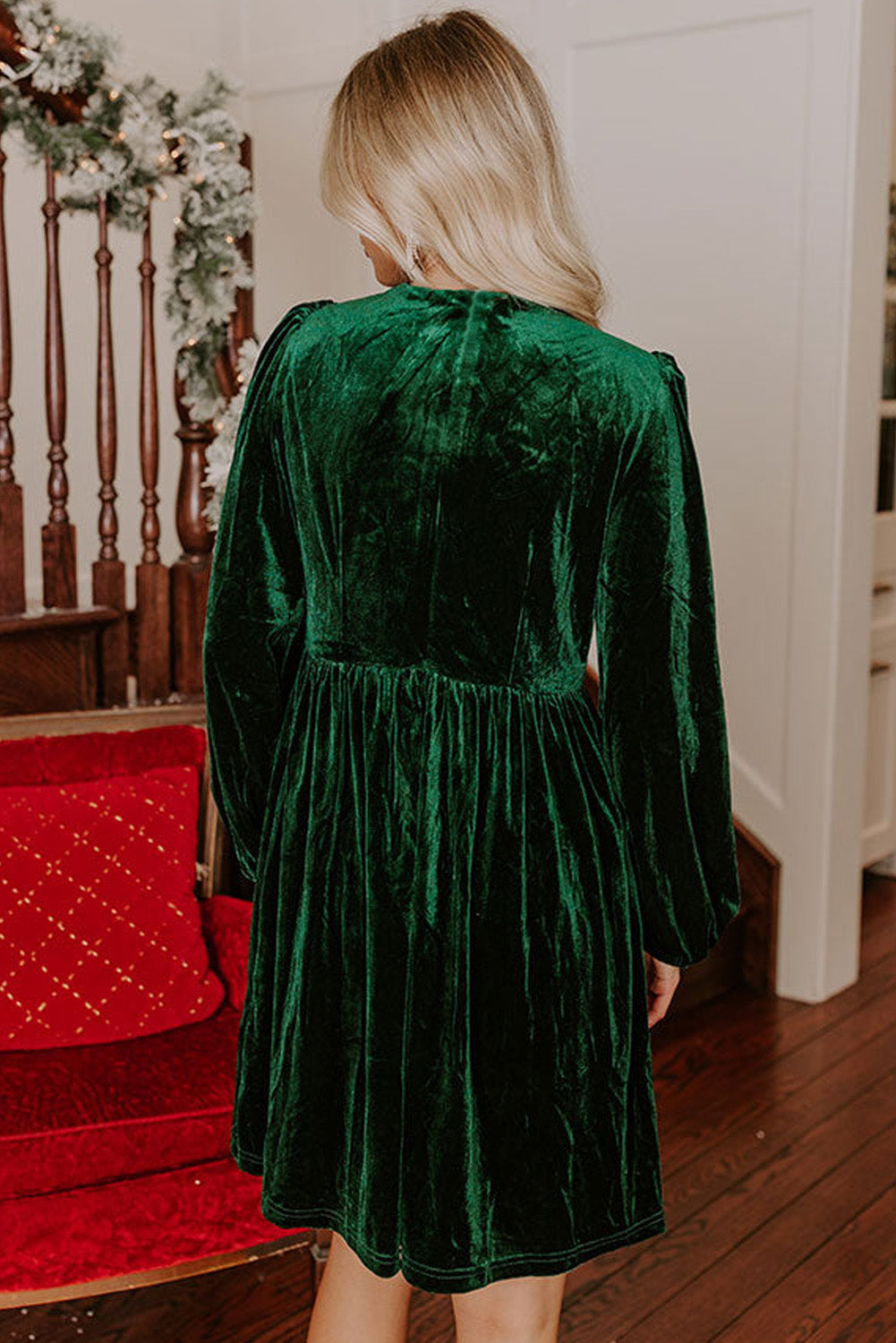 Woman in green velvet long sleeve dress, standing indoors by festive holiday decor