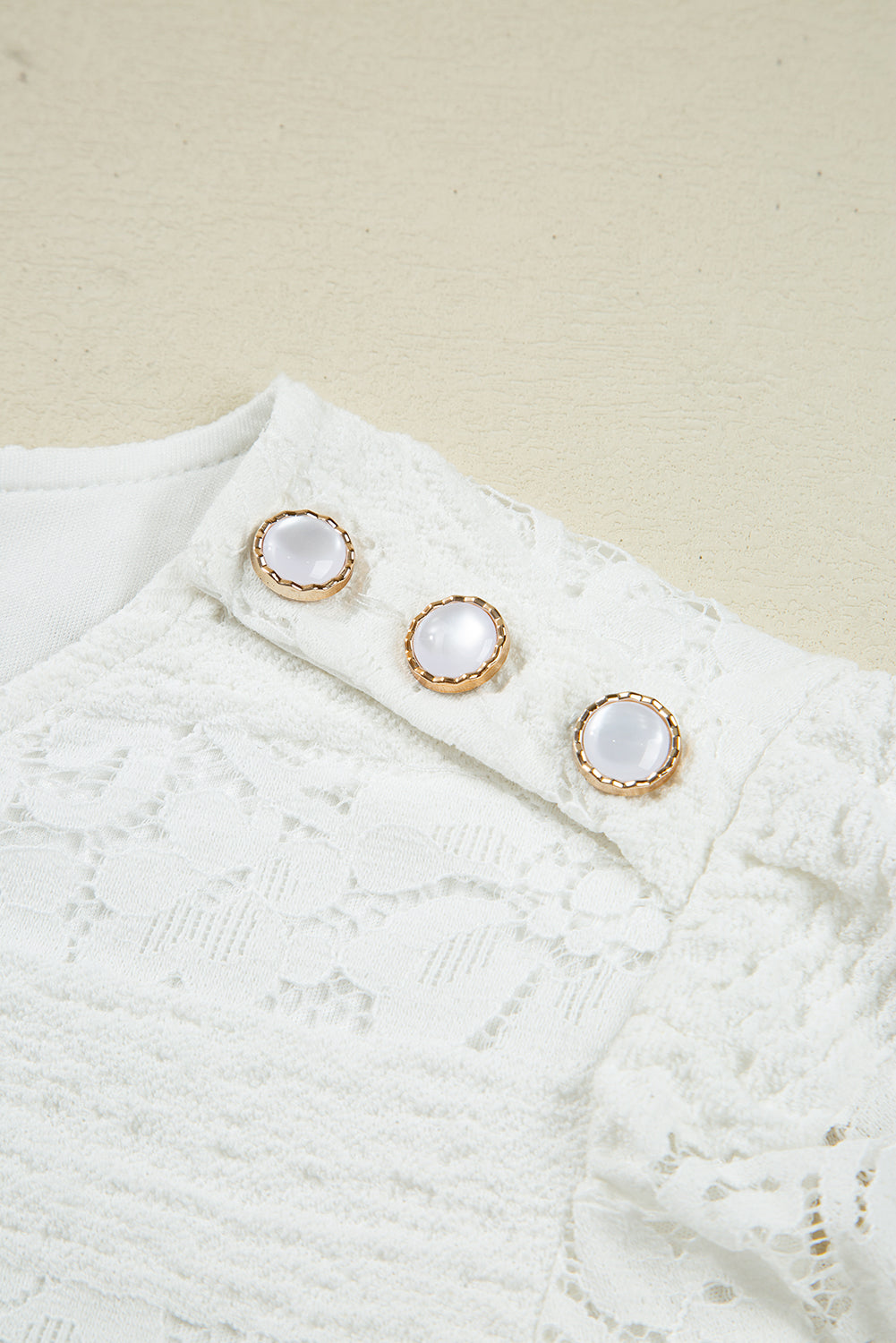White lace blouse shoulder detail with three pearl buttons and gold trim