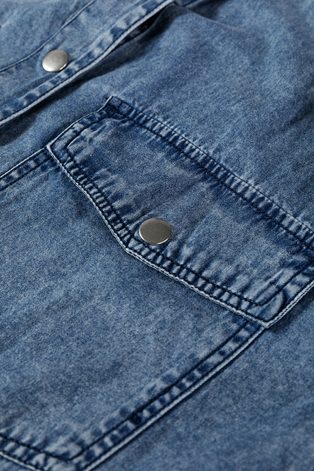 Close-up of blue denim jacket pocket with metal snap button and visible stitching