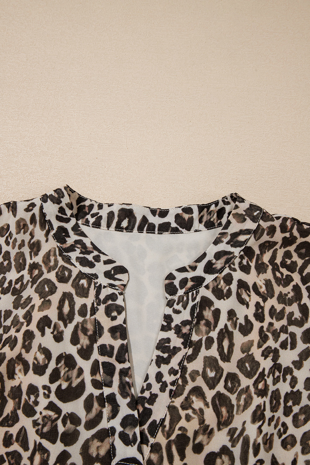 Close-up of a leopard print chiffon blouse with a notch neckline on a beige background