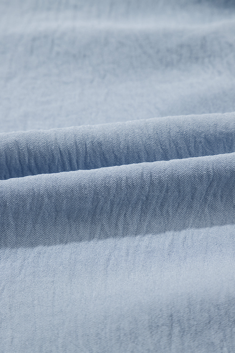 Closeup of soft light blue textured fabric with gentle folds, ideal for clothing or bedding