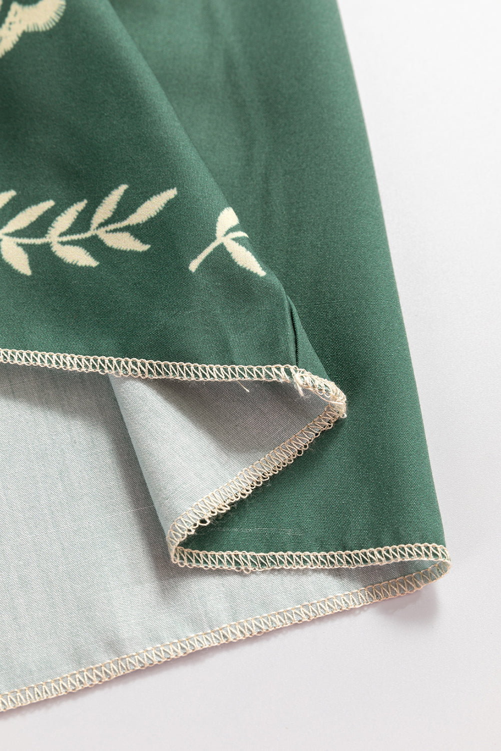 Close-up of green fabric with white leaf pattern and stitched hem, textile detail