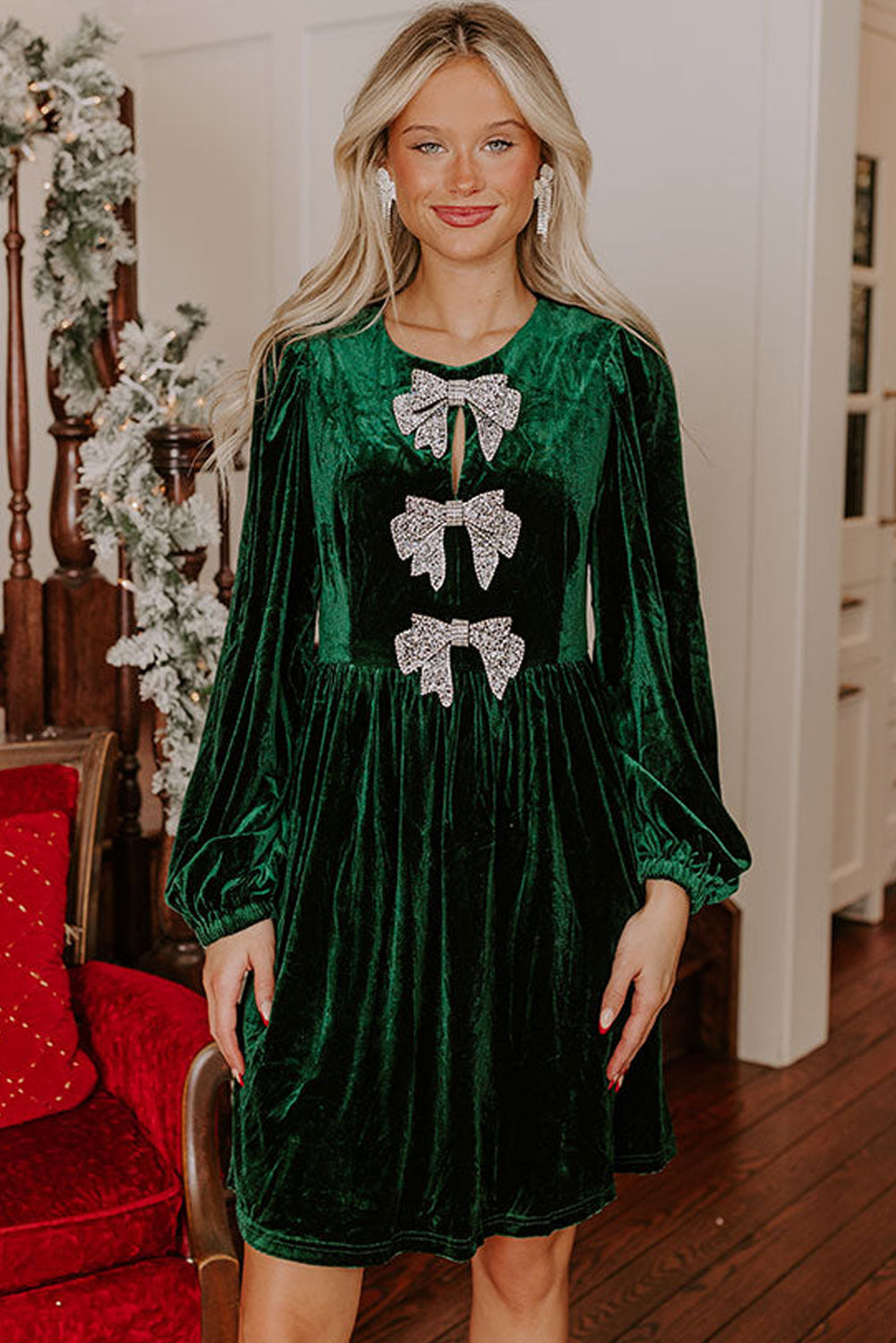 Woman wearing a green velvet dress with silver bow accents and long sleeves indoors