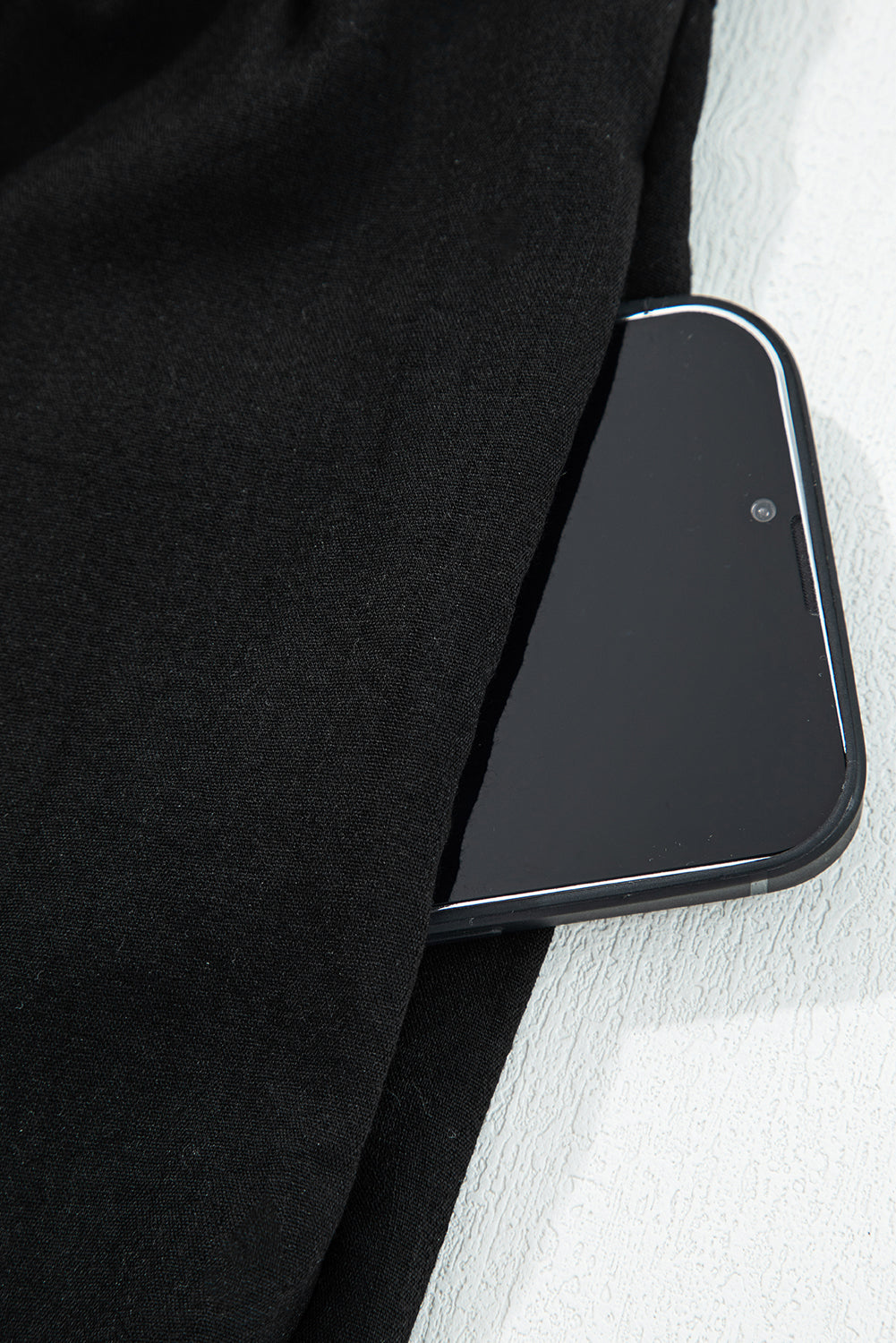 Smartphone in black pants pocket on a light textured surface