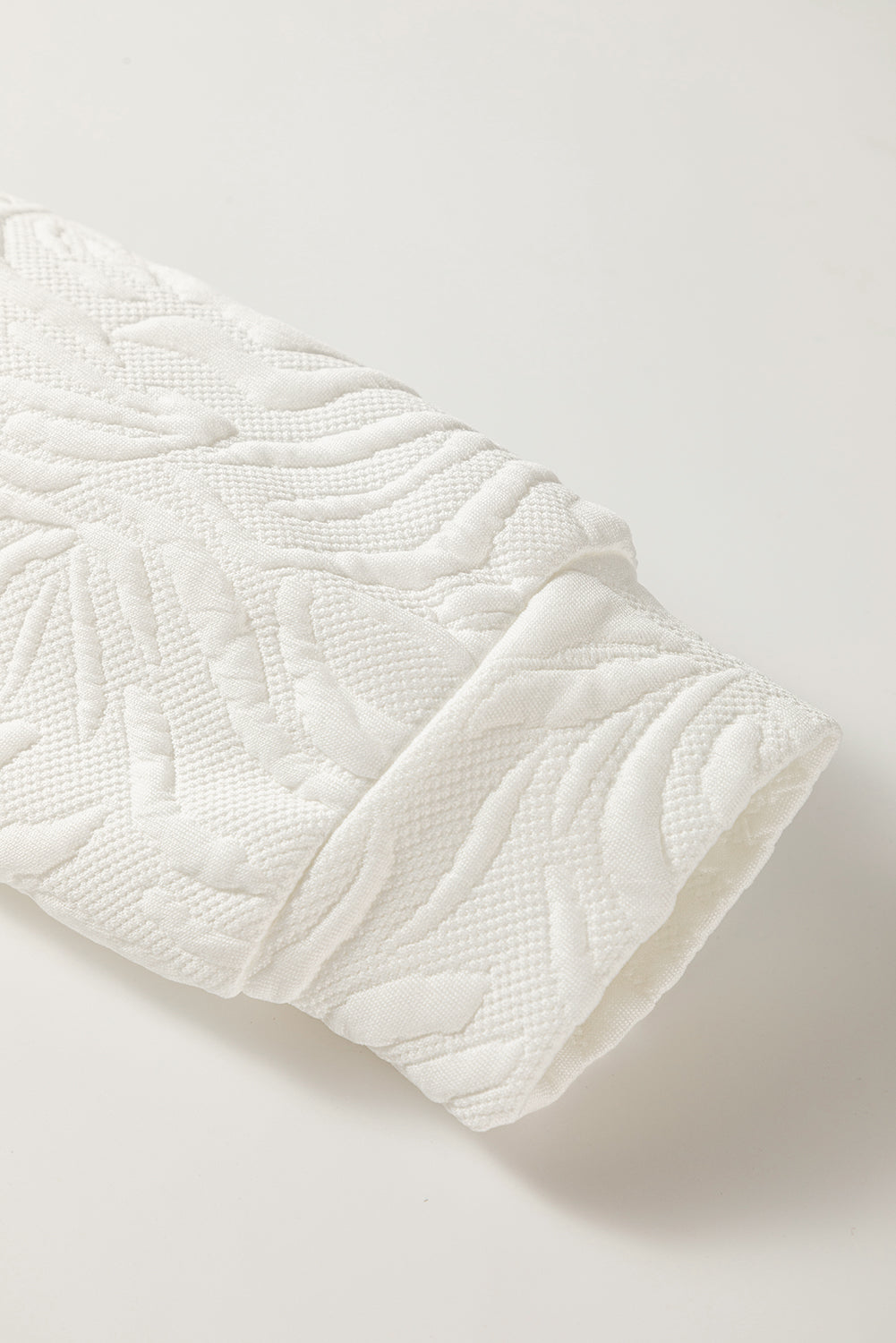 Close-up of textured white fabric sleeve with embossed leaf pattern on neutral background