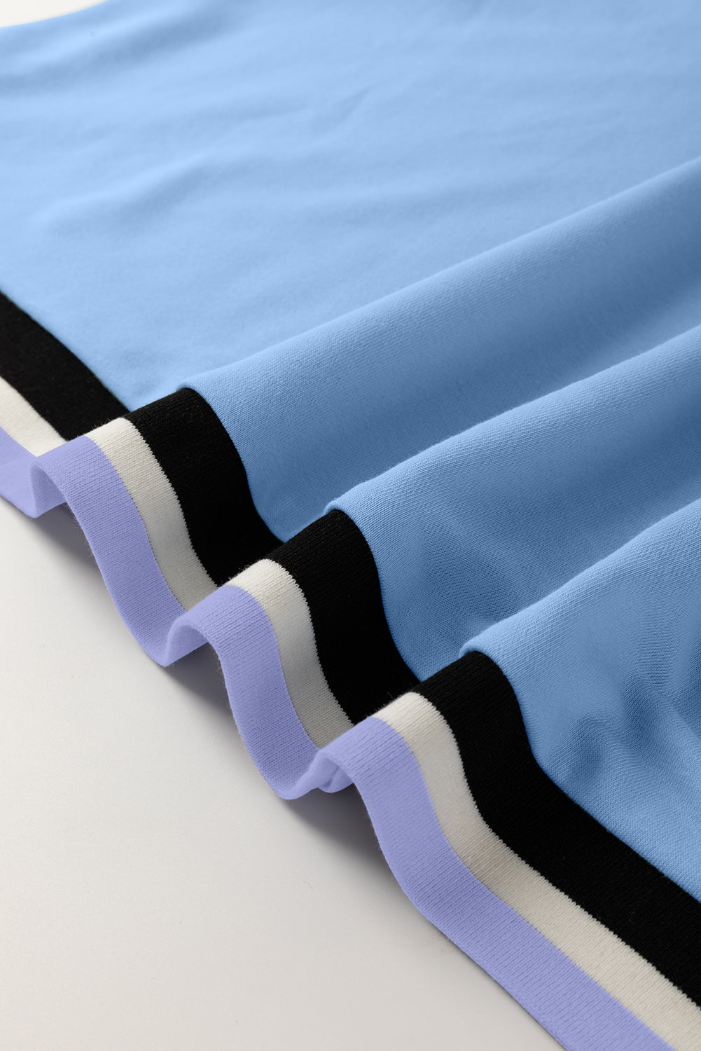 Light blue knit fabric with black, white, and purple striped hem detail, close-up