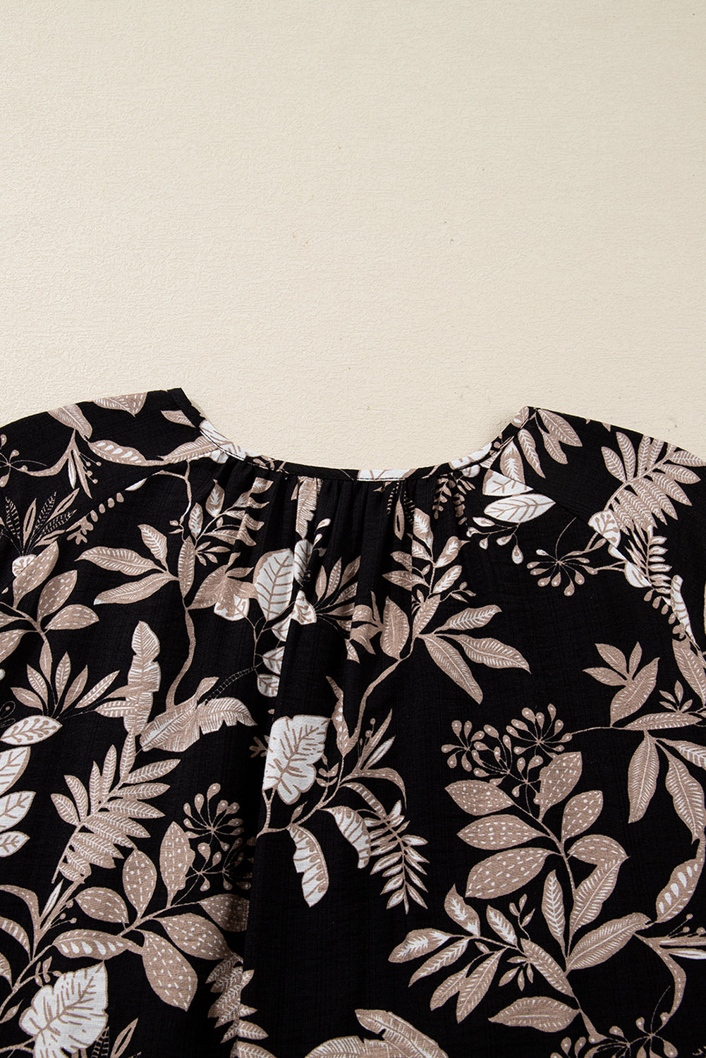 Black fabric with beige floral print design, close-up of gathered neckline detail