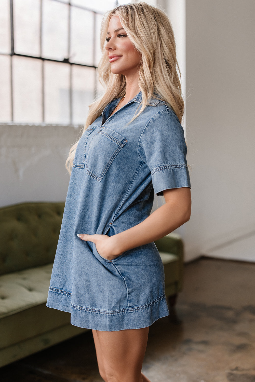Woman wearing a short sleeve denim dress with pockets, side view, in a modern room