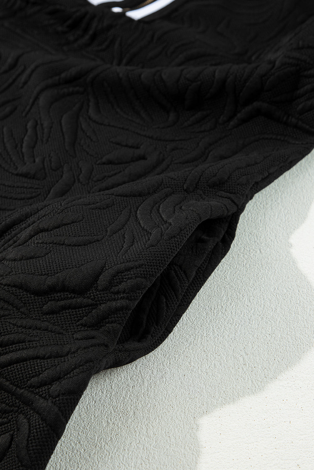 Close-up of black textured fabric with raised leaf pattern on a light surface