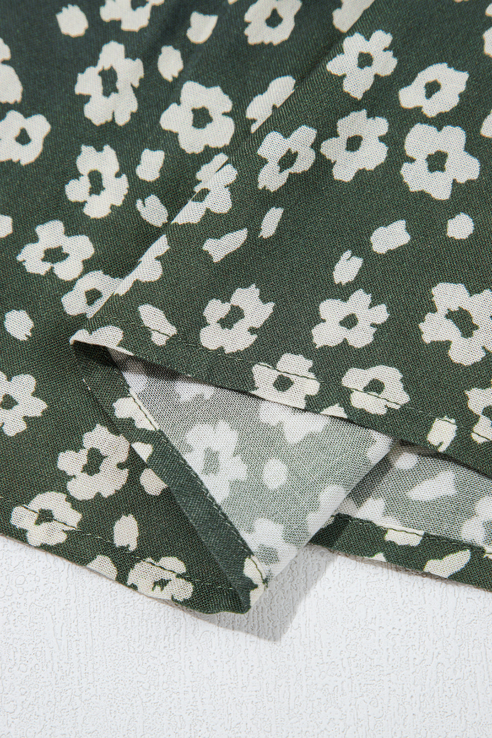 Green floral fabric with white flowers, close-up of hem and stitching detail