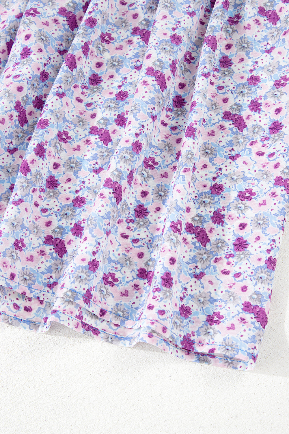 Close-up of light fabric with purple and blue floral print, soft pleated texture