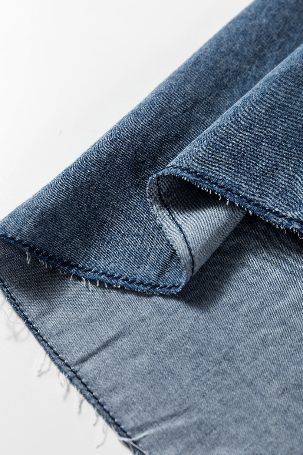 Close-up of blue denim fabric with visible stitching and frayed edges on white background