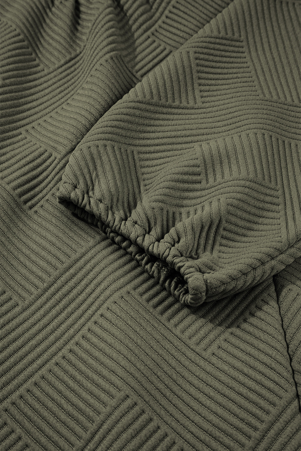 Close-up of textured olive green fabric with geometric ribbed pattern and elastic cuff