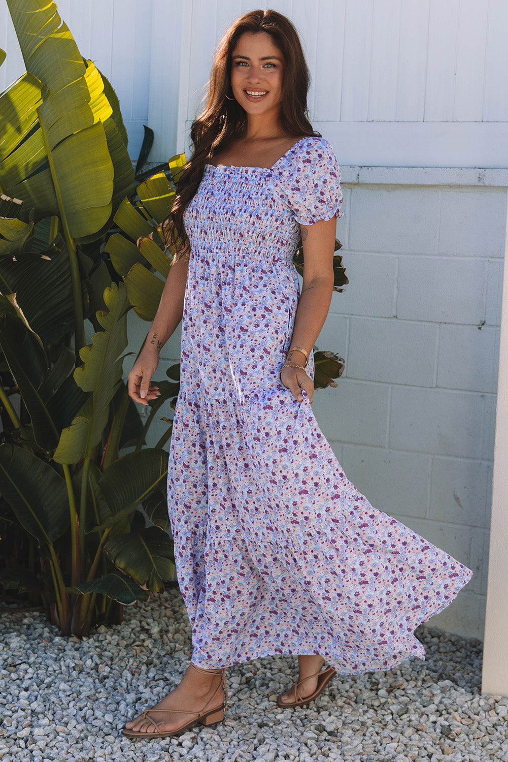 Woman in a long floral summer dress with puff sleeves, standing outdoors by green plants.
