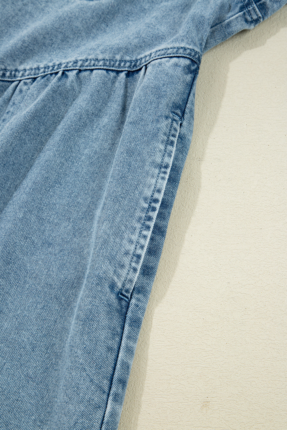Light blue denim garment sleeve with gathered seam on a beige background