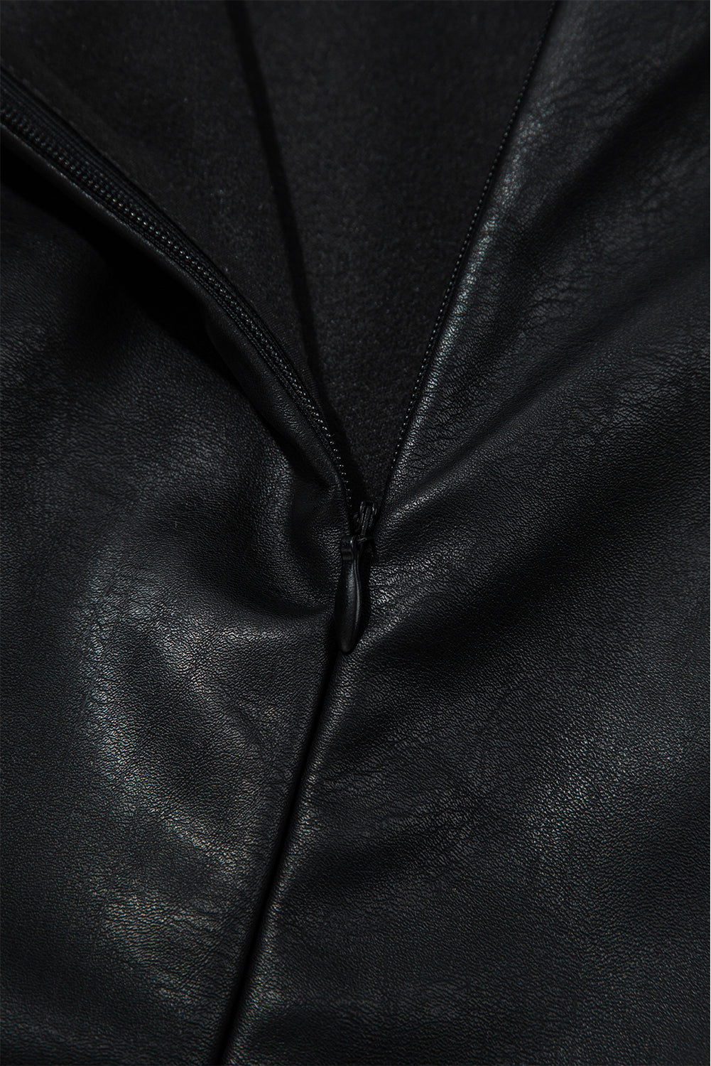 Close-up of black faux leather fabric with a zipper, textured surface detail