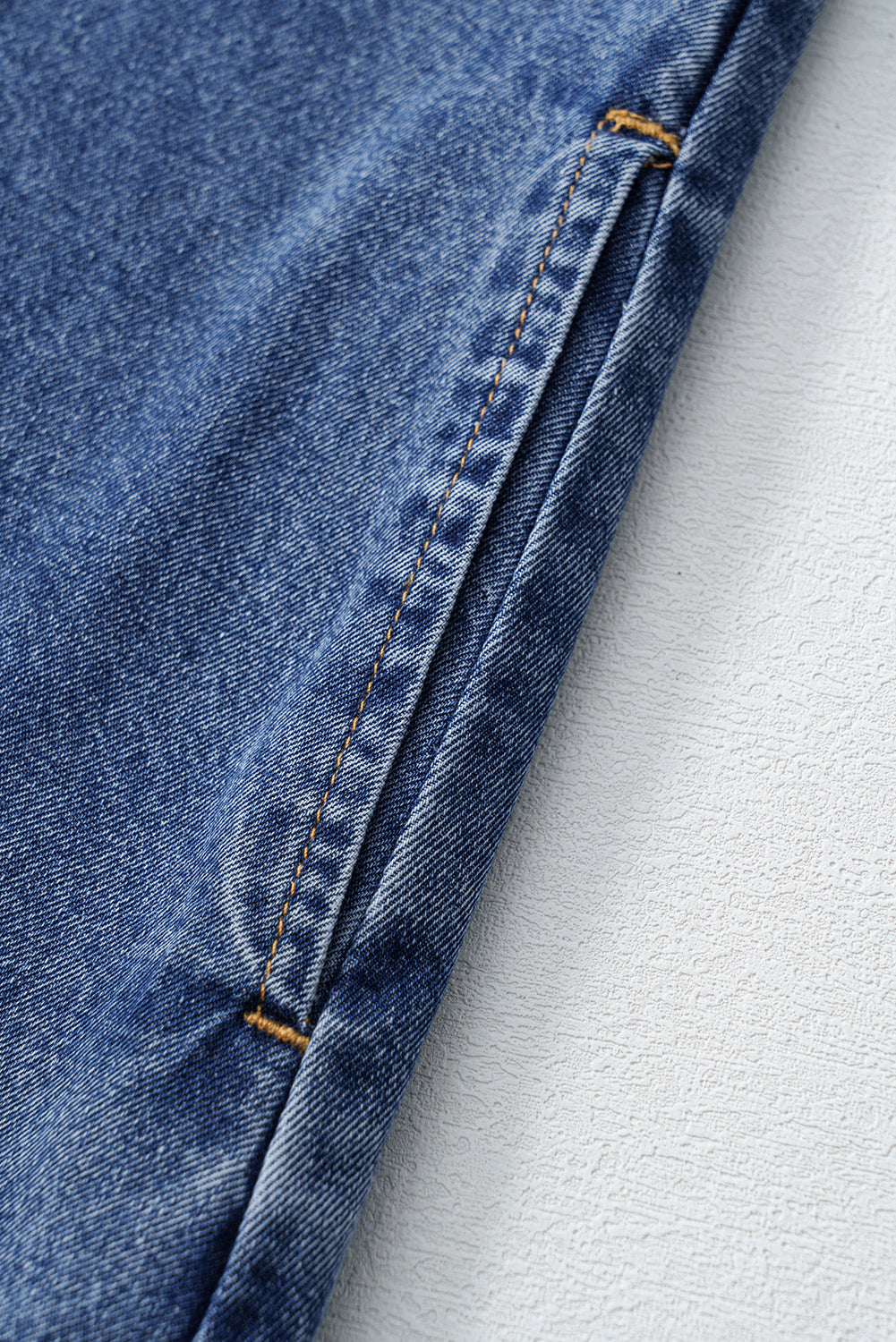 Close-up of blue denim jeans with detailed yellow stitching on textured white surface