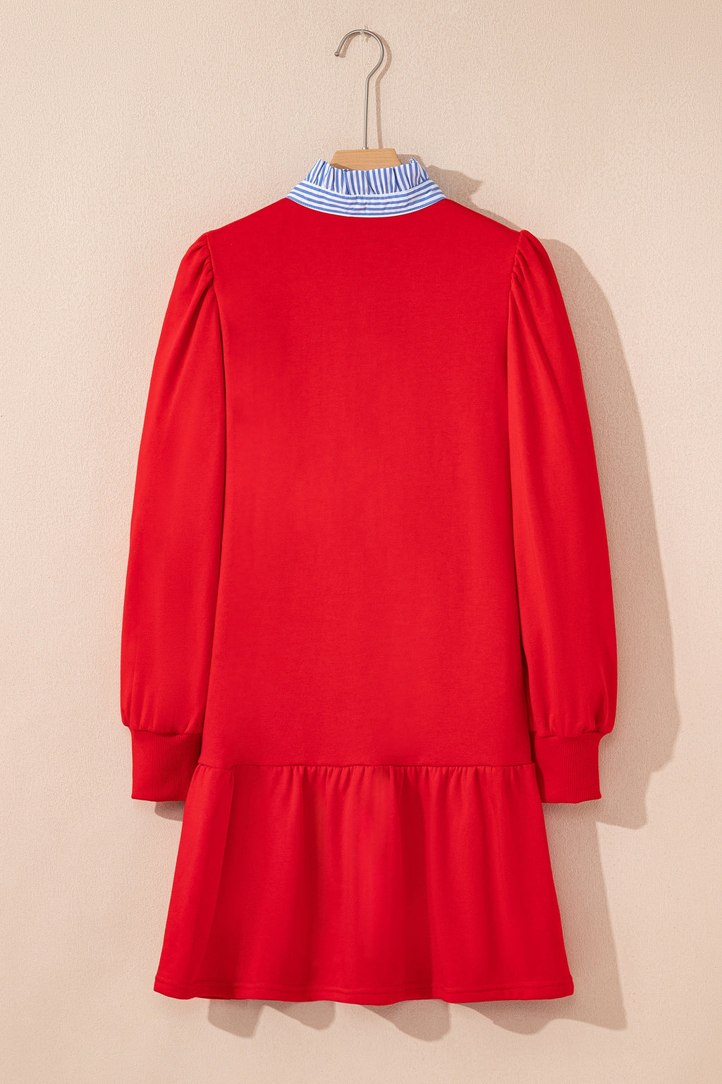 Red long sleeve dress with ruffled hem and blue striped collar, hanging on a wall.