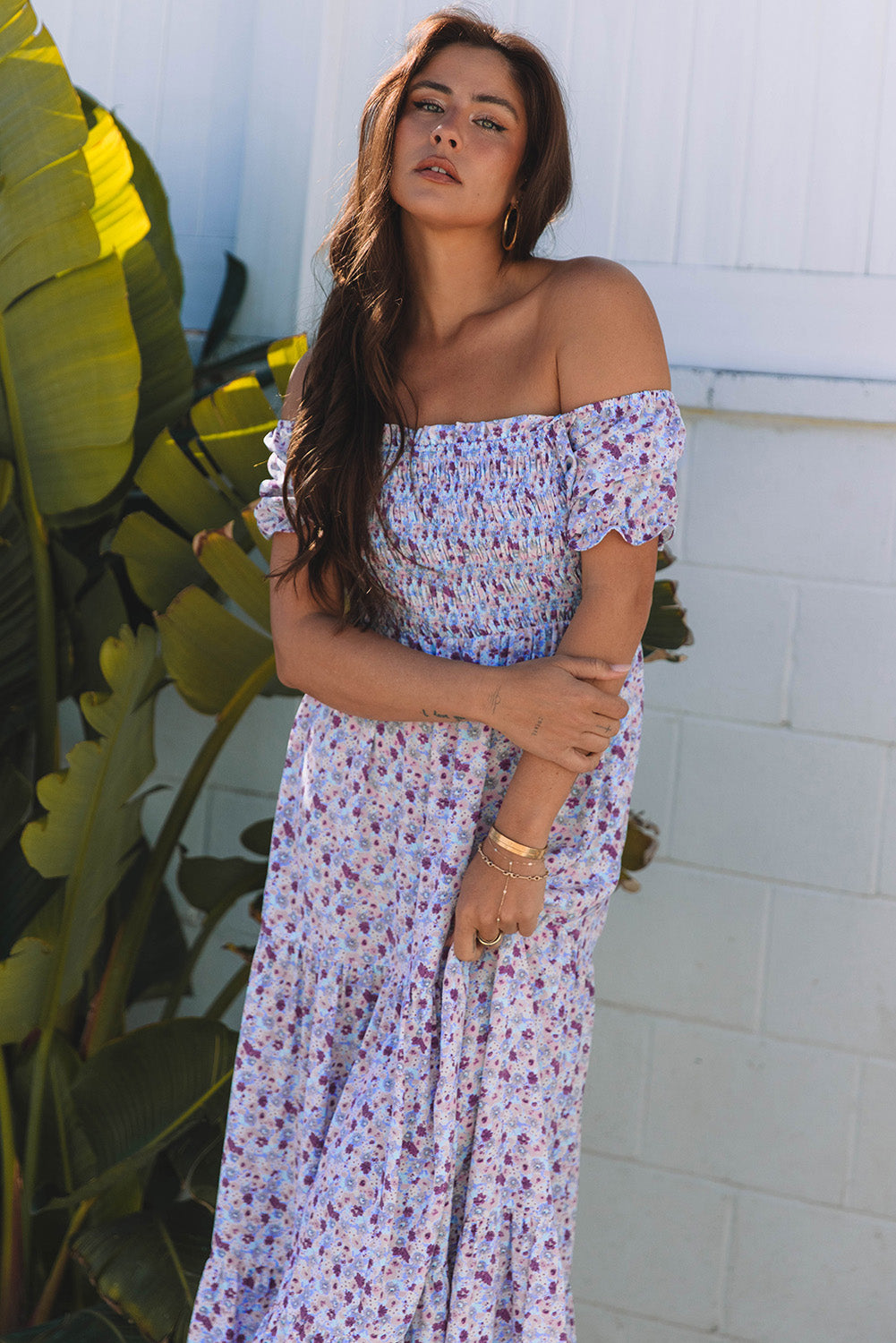 Woman wearing off-shoulder floral maxi dress, standing by green plants outdoors