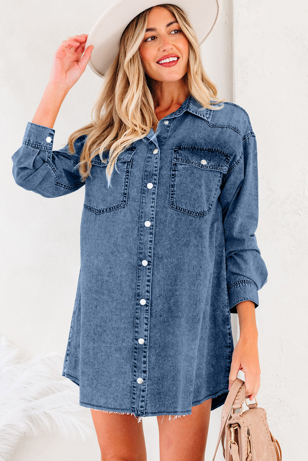 Woman in a casual denim shirt dress with long sleeves and front pockets, wearing a hat.