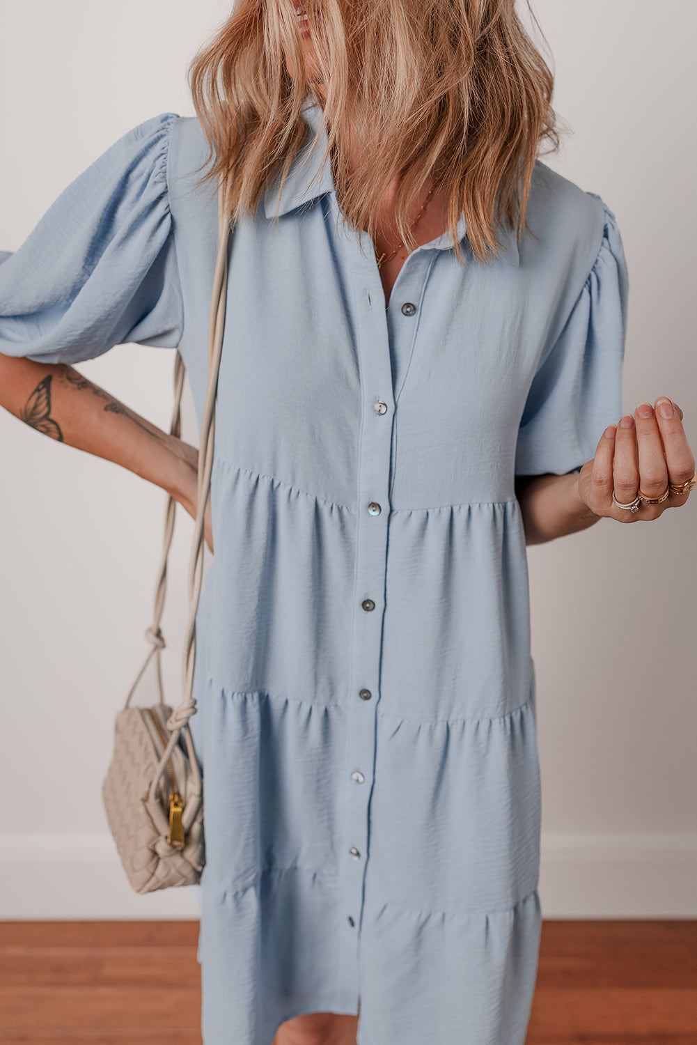 Woman wearing a light blue button-down short sleeve dress with a woven beige shoulder bag