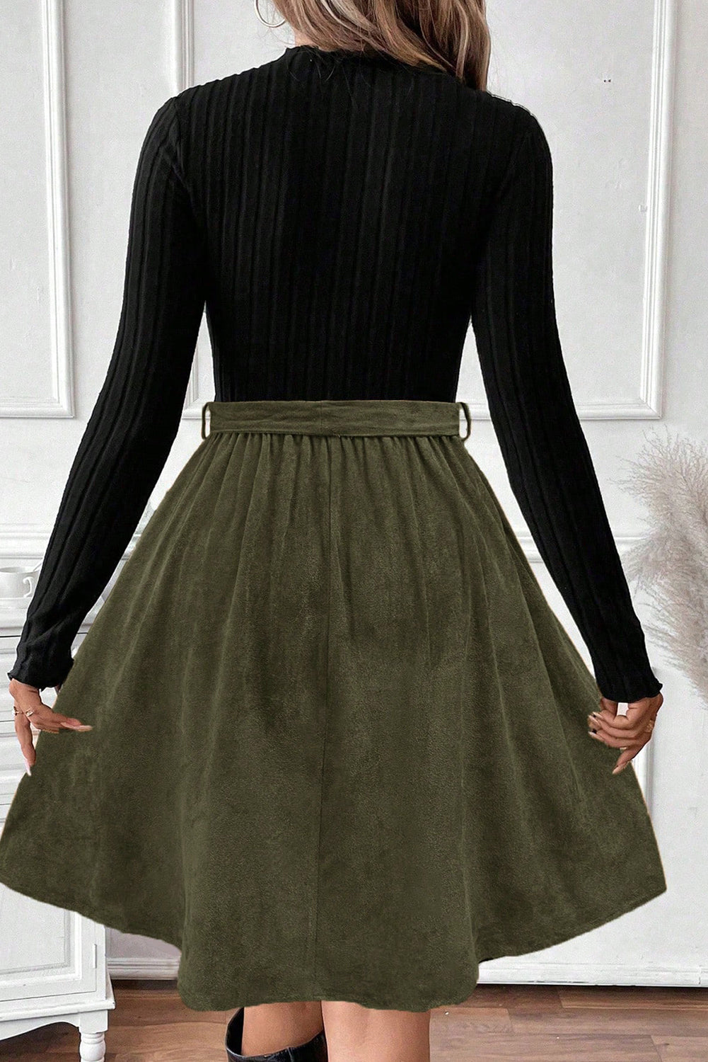 Woman in long sleeve black ribbed top and olive green flared skirt, back view, indoors