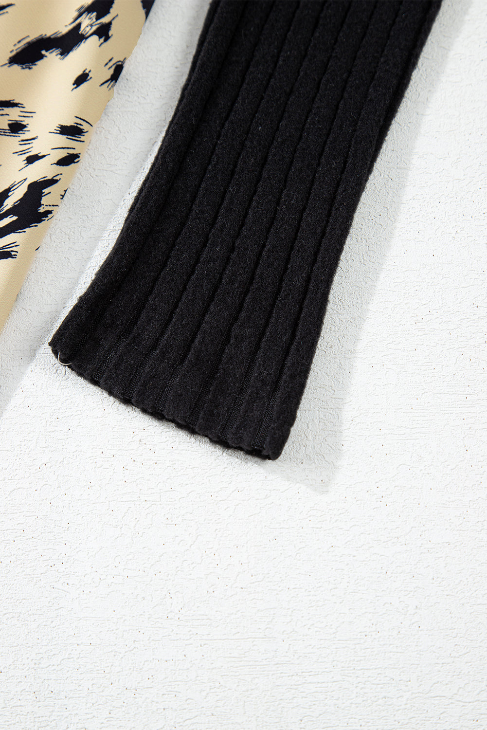 Close-up of a black ribbed knit sleeve and beige animal print fabric on a white surface