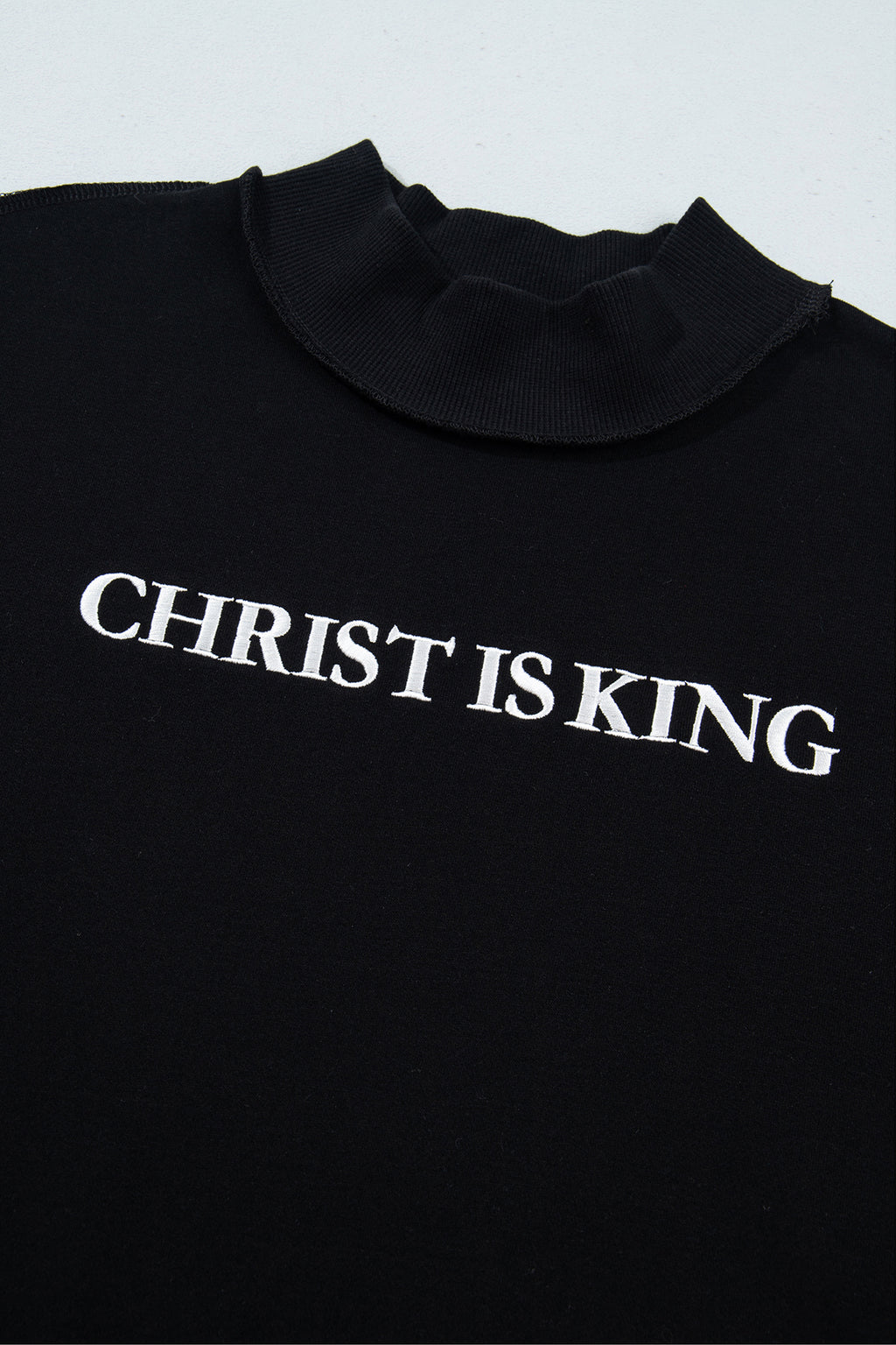 Черна блуза с поло яка и бял надпис CHRIST IS KING на гърдите, заснета отгоре
