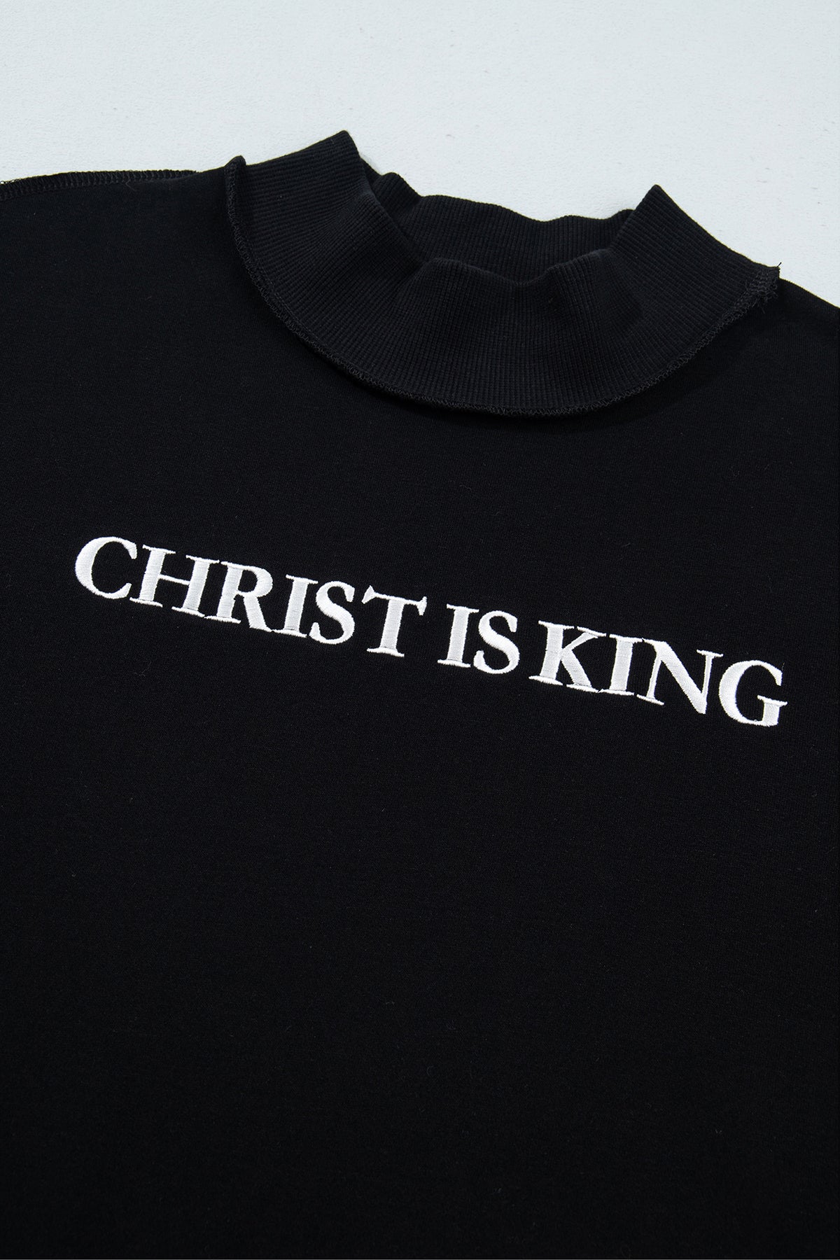 Черна блуза с поло яка и бял надпис CHRIST IS KING на гърдите, заснета отгоре
